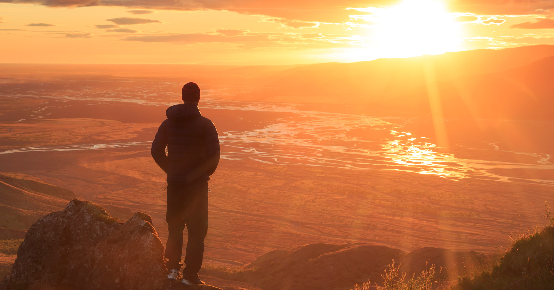 man standing on a cliff and looking off into the distance at a sunset